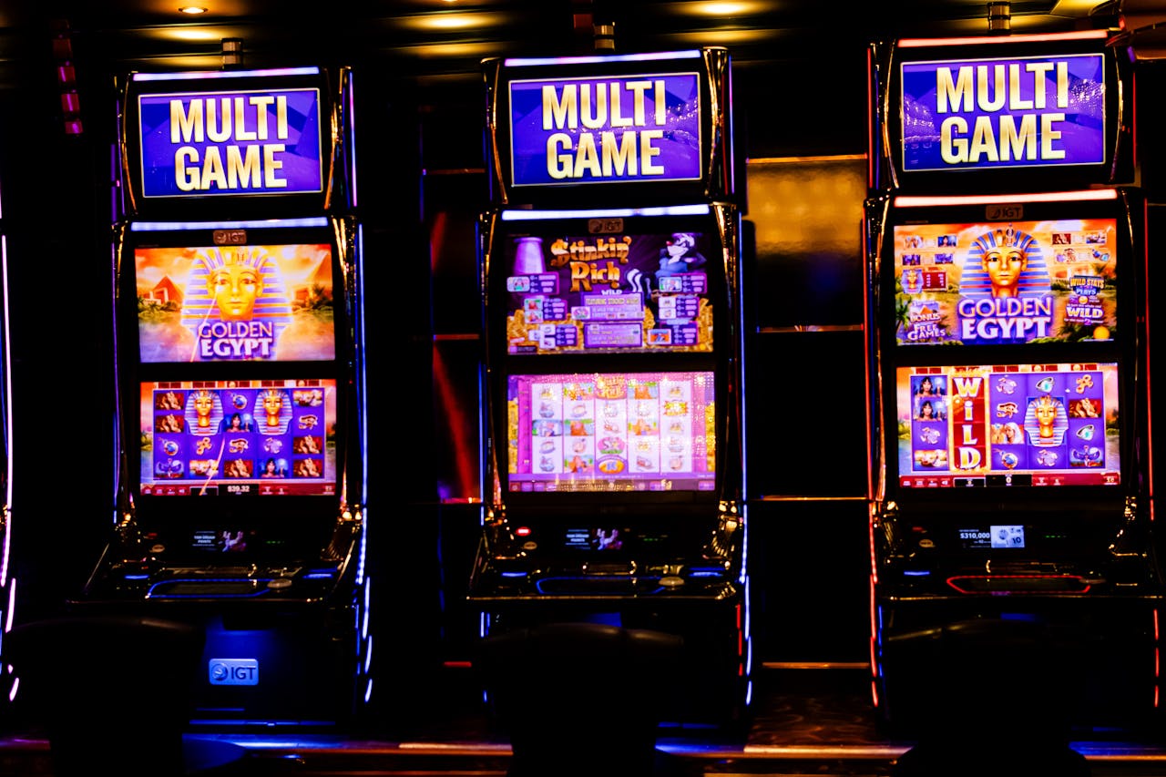 Three illuminated slot machines in a bustling casino at night.